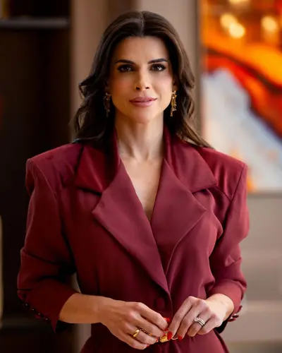 Mel Galhardo de blazer vinho, de frente, com as mãos unidas
